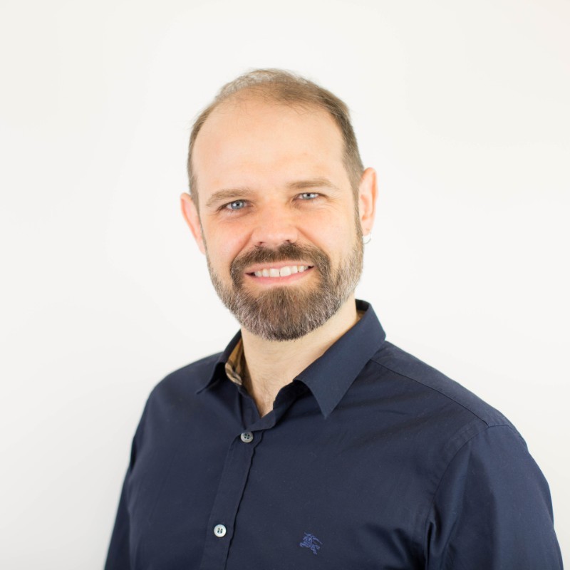 Professional headshot of a man in his 50s with grey hair, neutral studio background